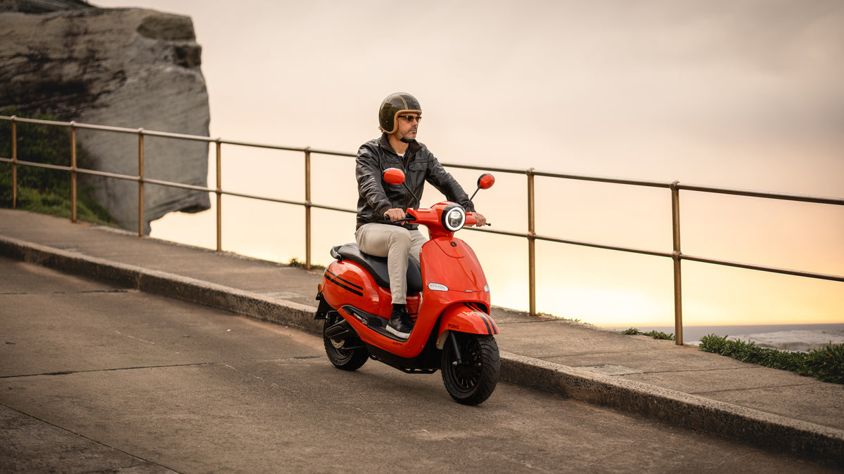 Rider on a red FONZ Z Series electric scooter riding a coastal road at sunset