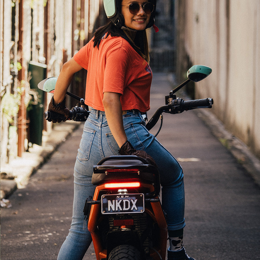 Woman sitting on a FONZ NKD X electric motorbike in a laneway, rear view