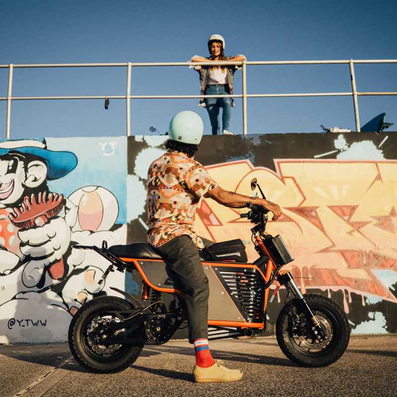 Rider on a FONZ NKD electric motorbike with integrated rear carrier in front of a street mural